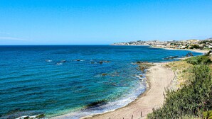 Vista costera con una playa arenosa, mar azul cristalino y un pueblo lejano.