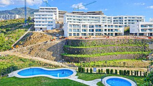 A modern hotel with multiple floors, a landscaped pool area, and construction cranes in the background. - Two Bedroom Apartment to rent in Carvajal (Fuengirola)
