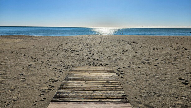 A wooden boardwalk leading to a beach with footprints in the sand. - Two Bedroom Apartment to rent in Carvajal (Fuengirola)
