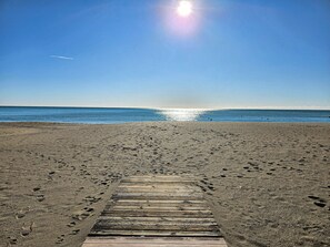 Ein hölzerner Steg führt zu einem Strand, im Sand sind Fußabdrücke zu sehen.