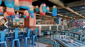 Ein Restaurant mit blauen Stühlen und Tischen, hängenden Leuchten und einem Wandgemälde.