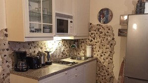 Eine kleine Küche mit weißen Schränken, einer Mikrowelle, einem Spülbecken und einem Kühlschrank.