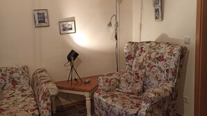 Ein Wohnzimmer mit zwei floralen Sesseln, einem Holztisch, einer Stehlampe und Wandregalen mit Dekoration.
