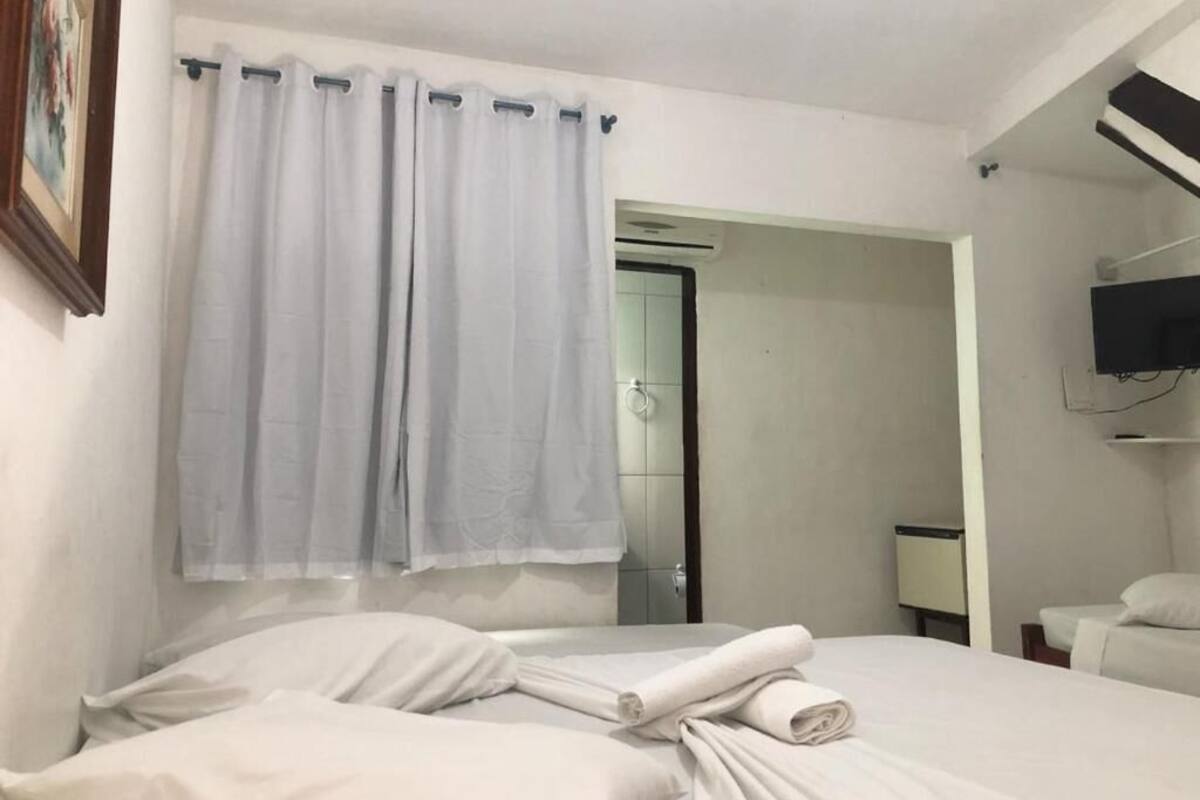 A hotel room with a bed, white curtains, a television, and a door leading to a bathroom.