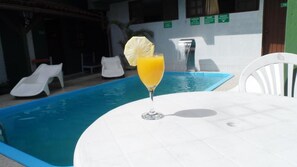 A poolside table with a glass of orange juice and a slice of pineapple.