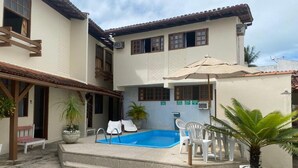 Un edificio de dos pisos con piscina, mobiliario exterior y plantas en macetas.
