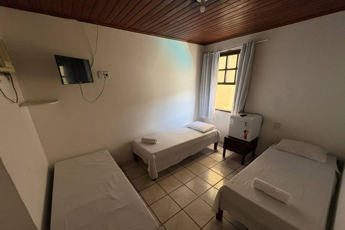 A room with two single beds, a small table, a heater, and a window with curtains.