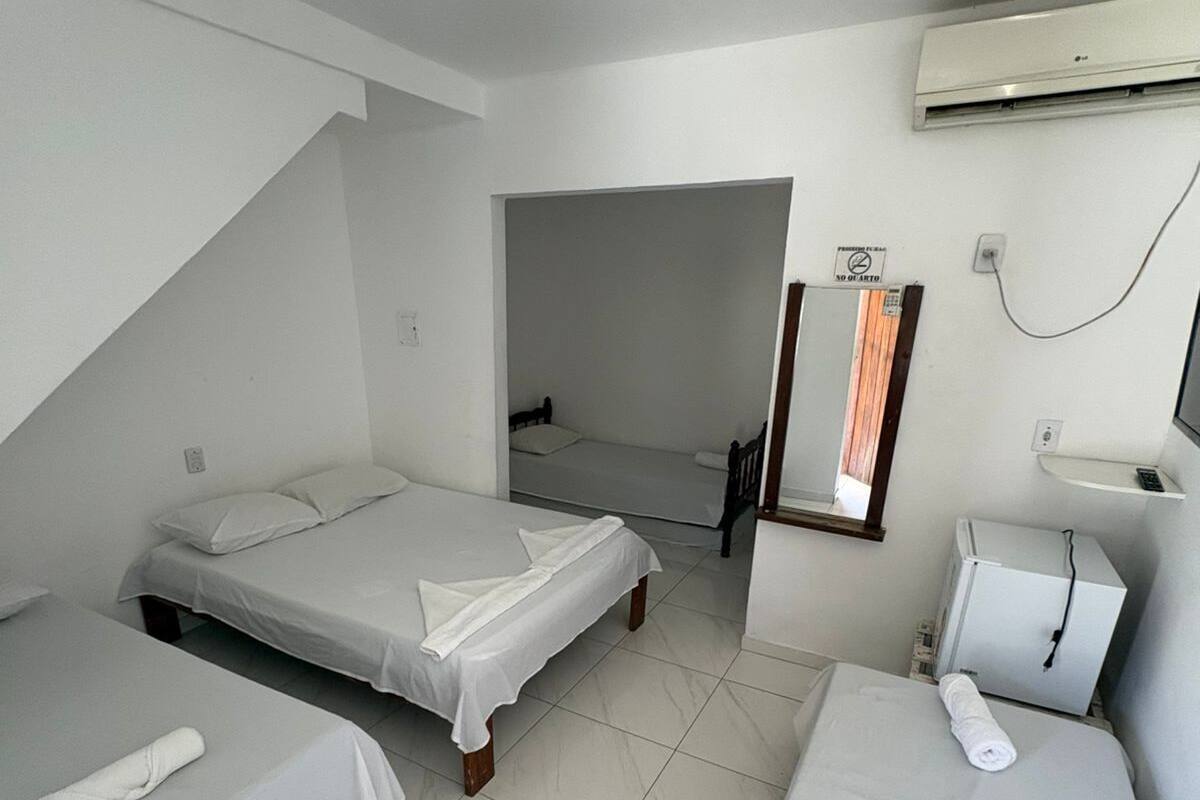 A small, clean room with two single beds, a small desk with a chair, a mirror, and an air conditioning unit.