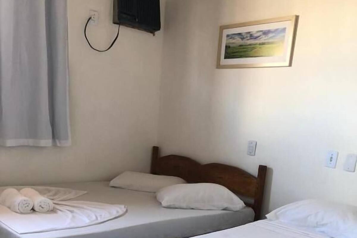 A room with two beds, each with white linens and pillows, a wooden headboard, a flat-screen TV mounted on the wall, and a framed picture above the beds.
