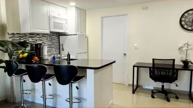 A modern kitchen with white cabinets, a black countertop, and a bar area with three black bar stools. - #34 Cozy in-law Port Richey Is an Entire Place (Port Richey)