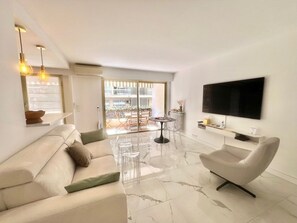Ein modernes Wohnzimmer mit einer Couch, einem Sessel, einem Fernseher und einem Glastisch.