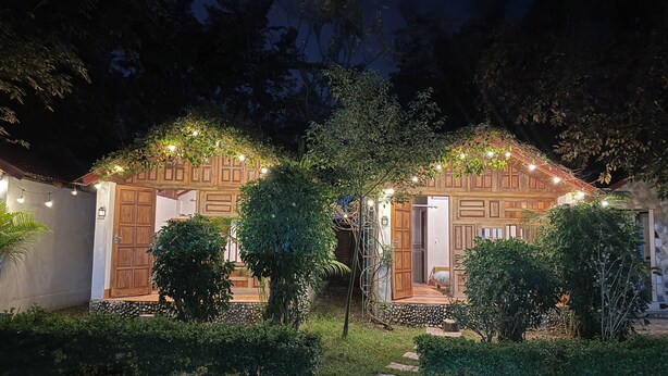 Une maison en bois à deux étages, avec une entrée donnant sur le jardin, entourée de verdure et illuminée de guirlandes lumineuses.