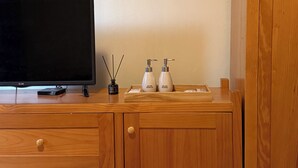 Un meuble en bois contenant un téléviseur à écran plat, un petit appareil noir et deux flacons blancs équipés de pompes.
