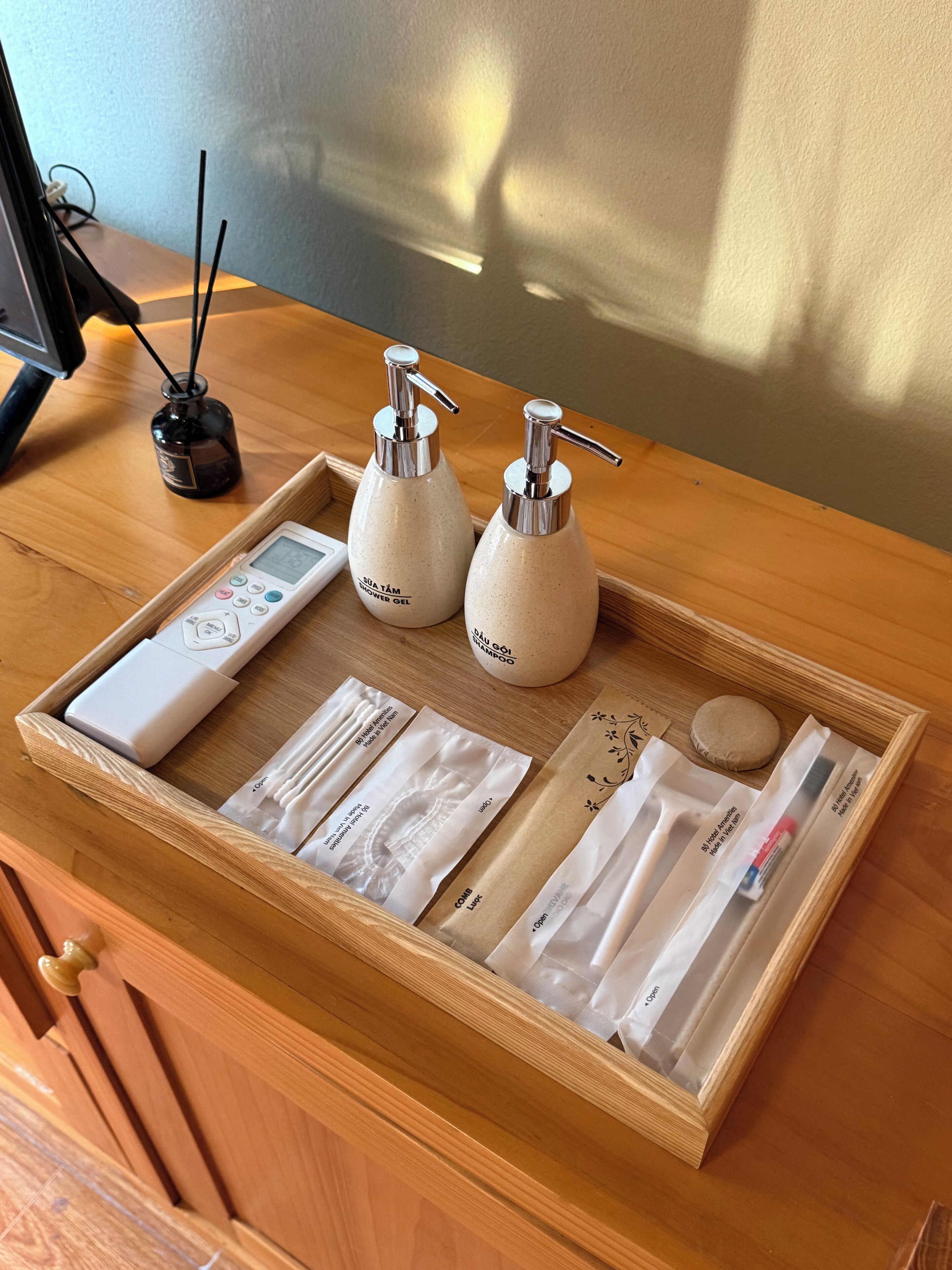 A wooden tray with toiletries including shower gel, shampoo, and combs, placed on a wooden surface.