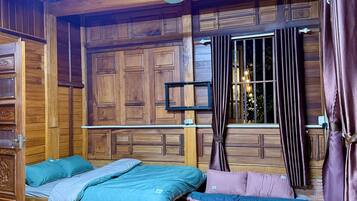 Una habitación con paneles de madera, ventilador de techo, cama con ropa de cama azul y rosa, y ventana con cortinas.