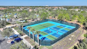 A tennis court surrounded by trees and a pool area.