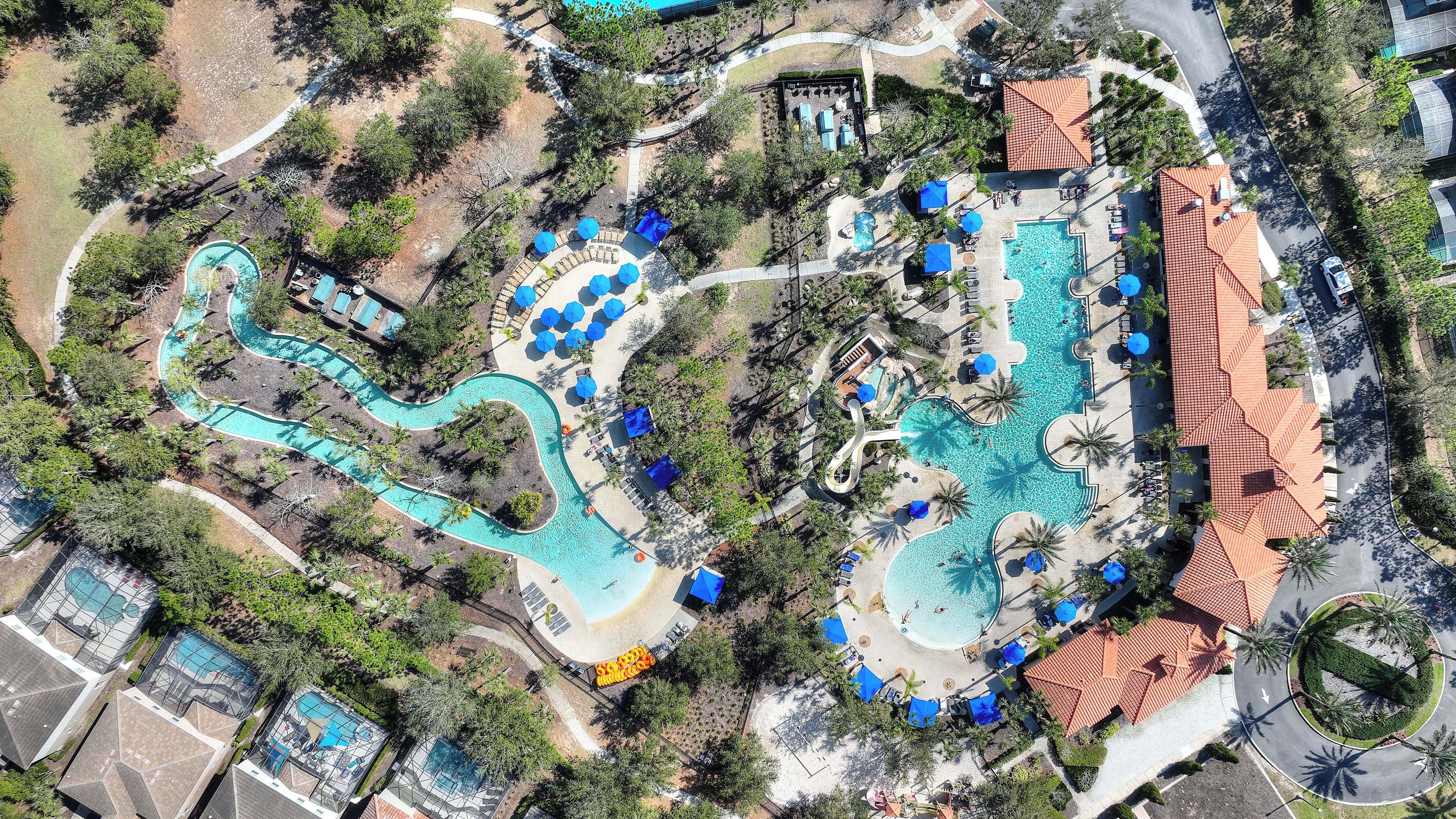 Vista aérea de un resort con varias piscinas, zonas de descanso y una fuente con recorrido sinuoso.