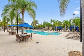 A pool area with lounge chairs and umbrellas, surrounded by palm trees.