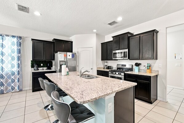 A modern kitchen with dark cabinetry, a granite countertop island, and stainless steel appliances. - 25% Off 5BR Retreat! Pool/Movie Room! (Davenport)