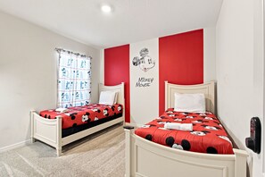 A bedroom with two beds, each with a Mickey Mouse themed bedspread, a red accent wall, and a Mickey Mouse wall decal.