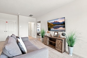 A modern living room with a grey sofa, a flat-screen TV mounted on the wall, and a wooden entertainment unit.