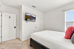 Ein Schlafzimmer mit einem Bett, einem an der Wand befestigten Fernseher und einer Tür mit der Nummer 5.