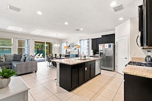 A modern kitchen with a central island, built-in appliances, and a dining area with a sofa and chairs. - 25% Off 5BR Retreat! Pool/Movie Room! (Davenport)