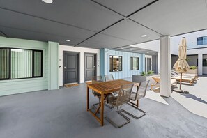 Un espace de restauration extérieur moderne, avec une table en bois et des chaises en métal, entouré de fauteuils et de parasols.