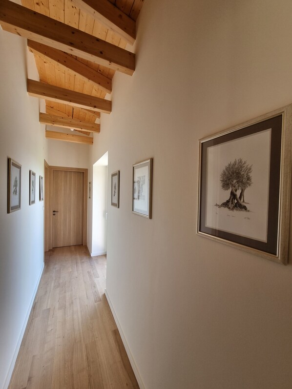 A hallway with wooden beams, framed artwork on the walls, and a wooden door at the end.