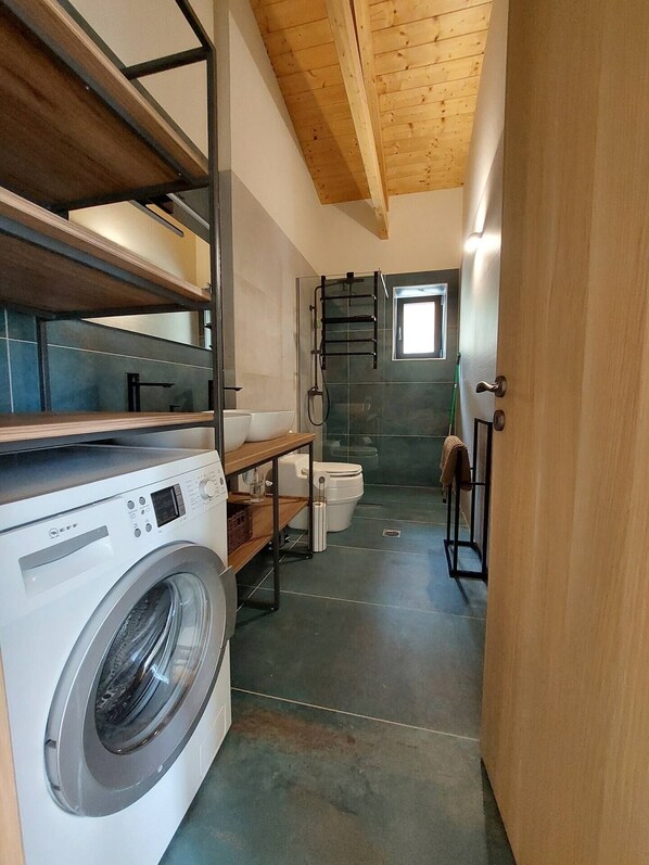 A compact laundry room with a washing machine, a drying rack, and a toilet.
