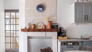 A kitchen with a brick wall, a shelf with pottery, a radio, and a dining area with a table and chairs. - Gite de la Closerie – Independent Country House, Perfect for Families (Oisly)