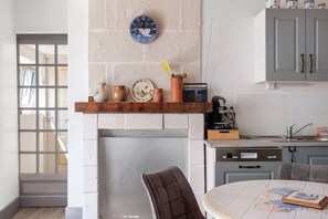 A kitchen with a brick wall, a shelf with pottery, a radio, and a dining area with a table and chairs. - Gite de la Closerie – Independent Country House, Perfect for Families (Oisly)