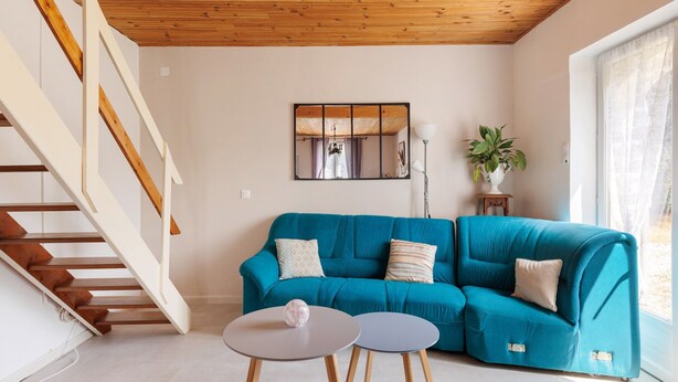 A living room with a teal sofa, a staircase, a mirror, and a potted plant. - Gite de la Closerie – Independent Country House, Perfect for Families (Oisly)