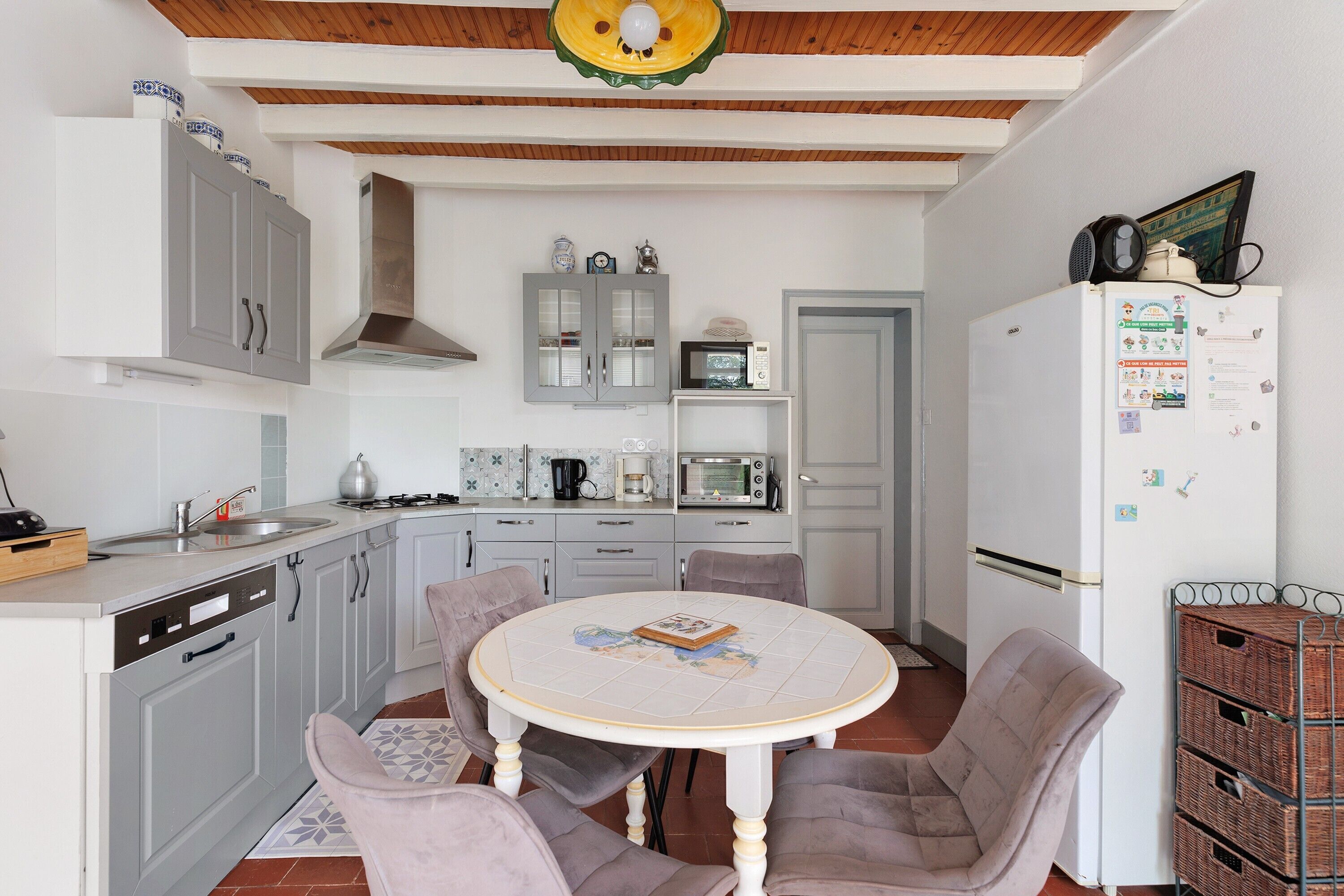 A kitchen with grey cabinets, a white dining table with chairs, a microwave, and a refrigerator.