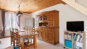 A dining area with a wooden table and chairs, a wooden cabinet, and a television on a stand. - Gite de la Closerie – Independent Country House, Perfect for Families (Oisly)