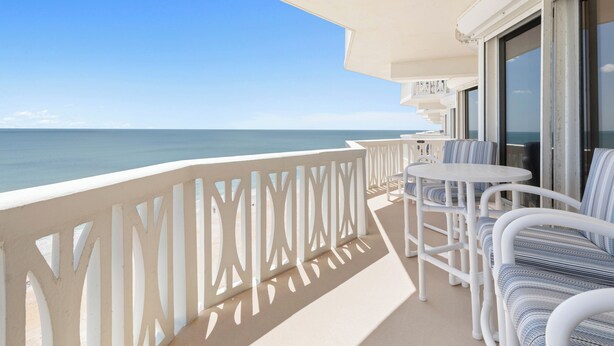 A balcony with a view of the sea, white outdoor furniture, and a glass door leading to an interior space. - New listing! 3-bedroom. Ocean-Front, Corner Unit with Panoramic Views (Ormond Beach)