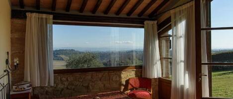 Una habitación con una cama, una silla, una maleta y vistas al campo.