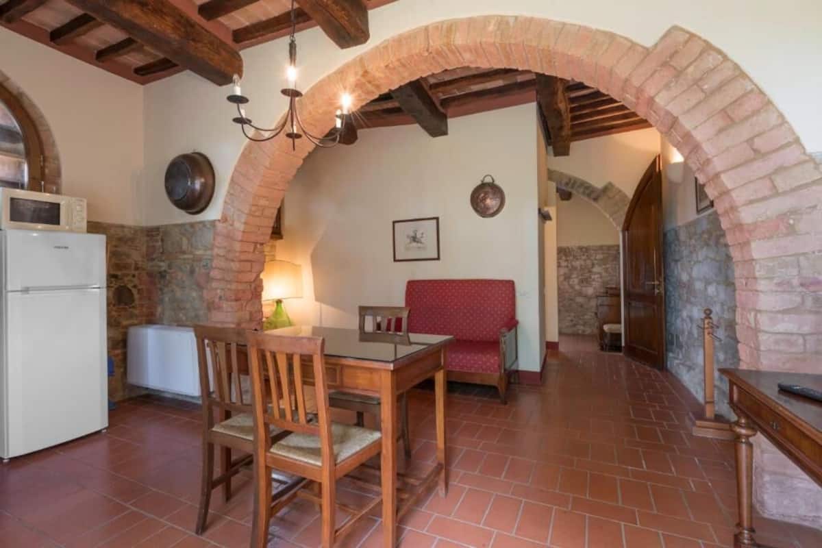 A rustic kitchen with a wooden table and chairs, a white refrigerator, and a stone wall.