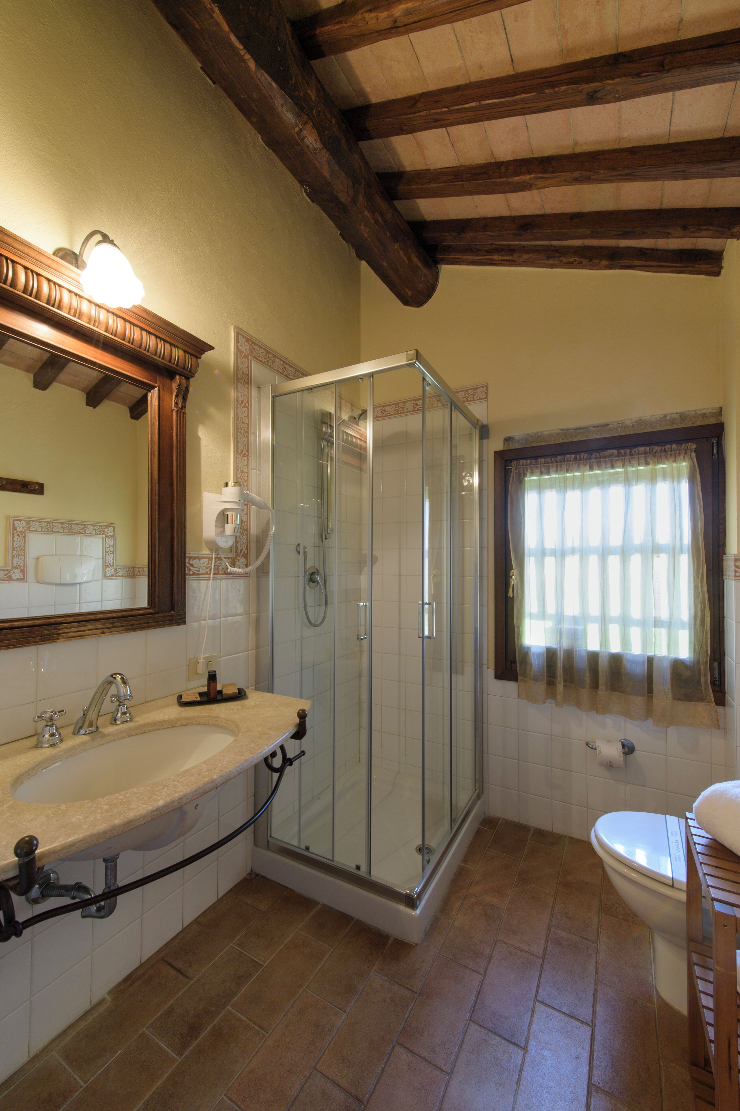 A bathroom with a shower, sink, toilet, and a window with curtains.