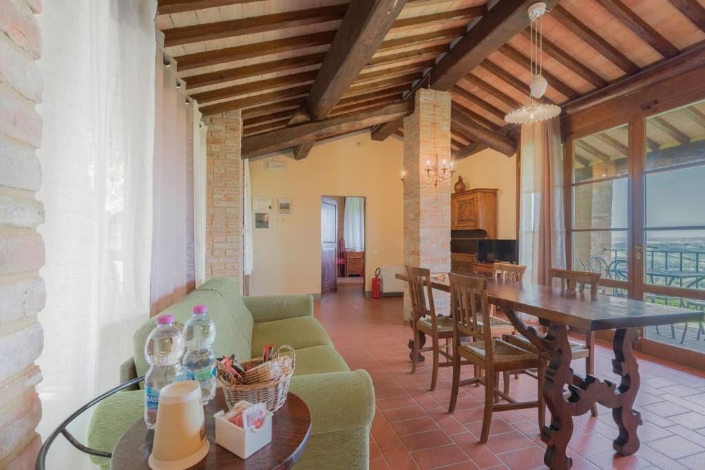 A spacious living area with a green sofa, wooden dining table, and chairs, a fireplace, and large windows.