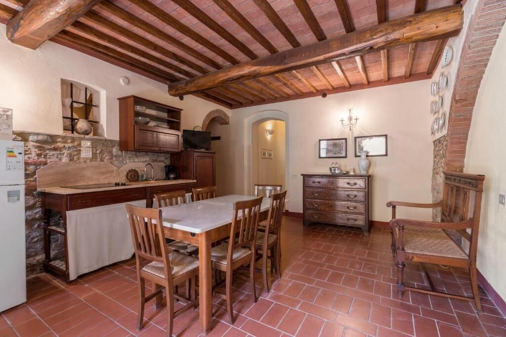 Eine rustikale Küche mit Holzbalken, einer Steinwand, einem Esstisch mit Stühlen und einem Holzschrank.