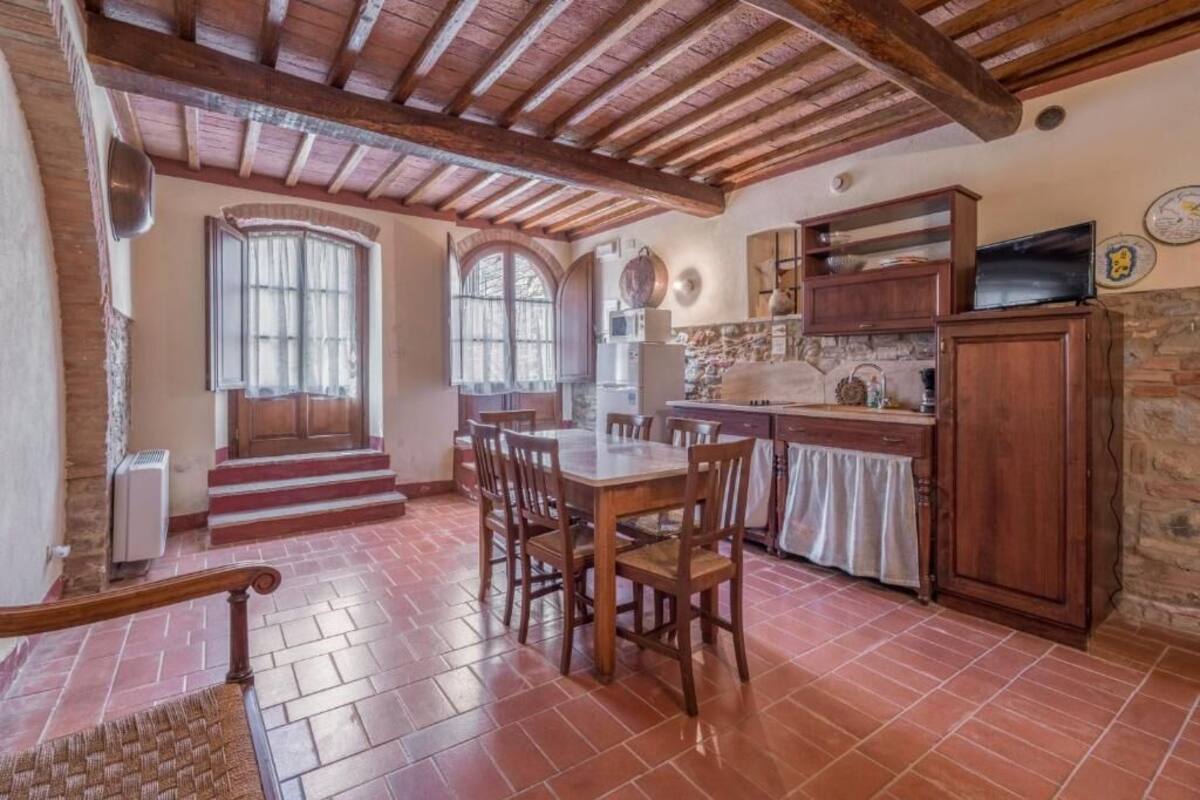 A rustic kitchen with wooden beams, a dining table with chairs, and a stone wall.