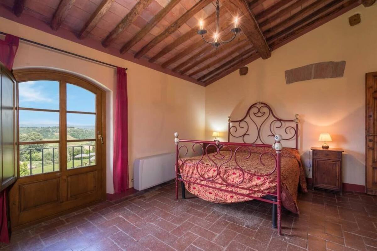 A bedroom with a bed, a chandelier, a wooden door, and a view of the outdoors.