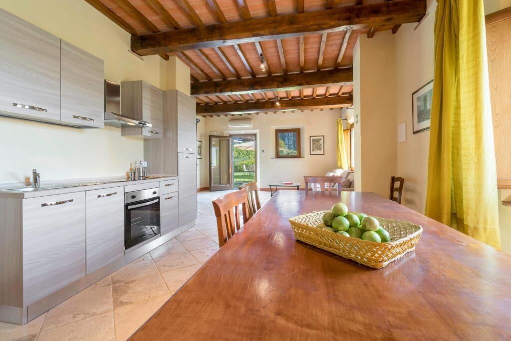 A kitchen with modern appliances, a dining table with chairs, and a basket of fruit.