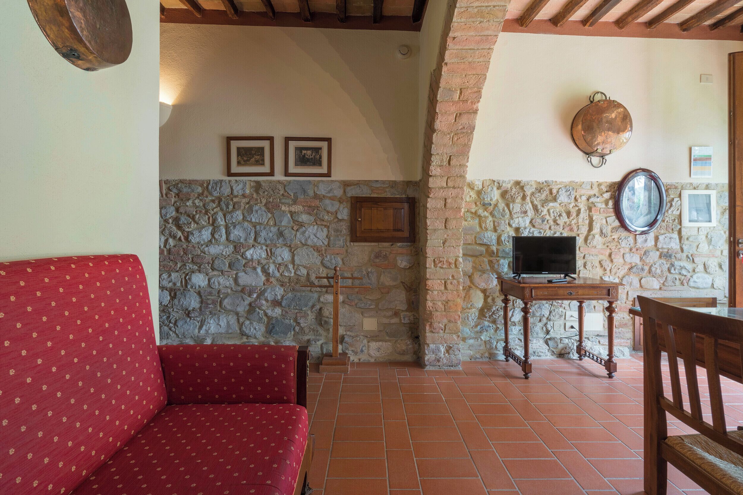 Una sala de estar acogedora con un sofá rojo, pared de piedra, mesa de madera con un televisor y una chimenea de piedra.