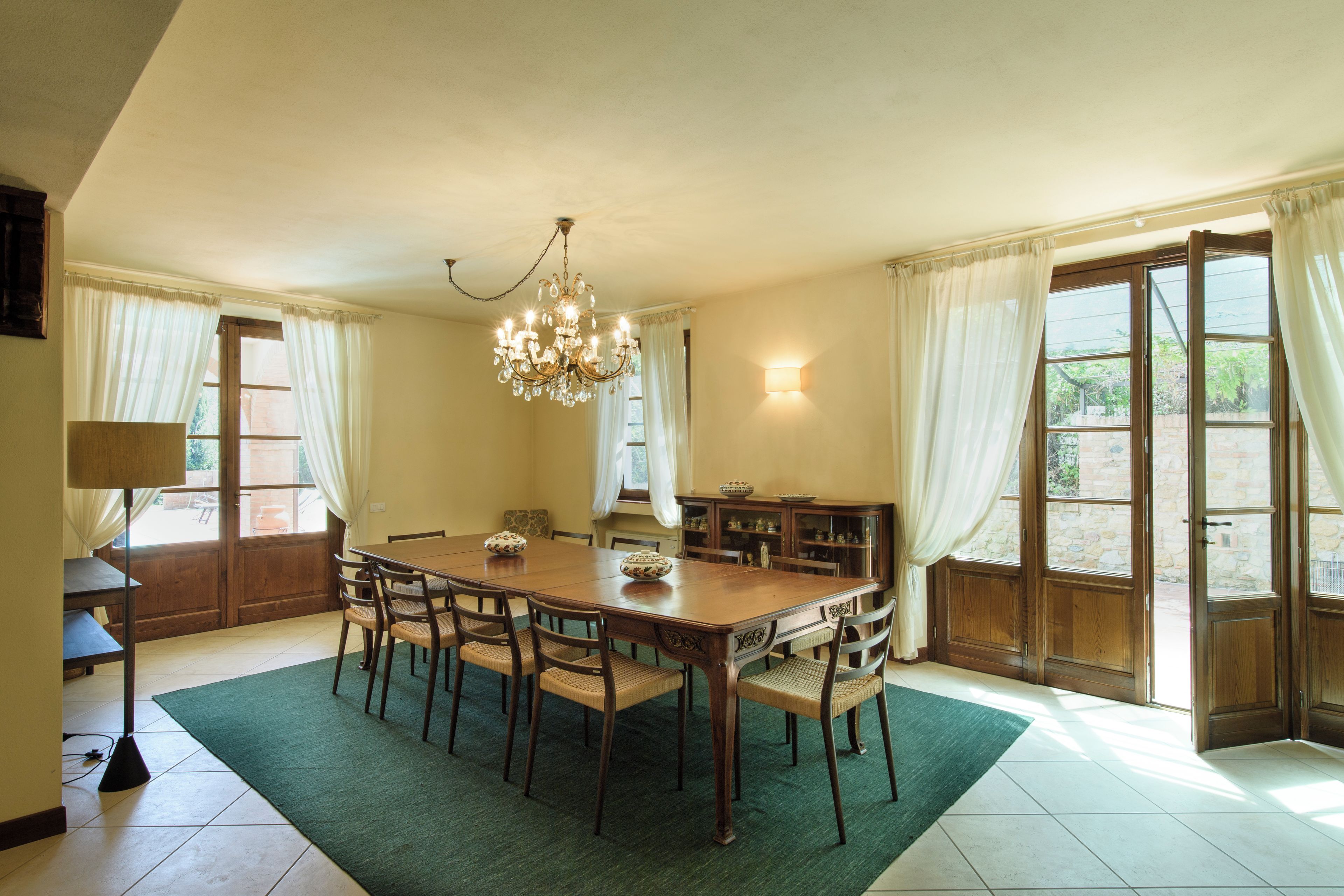A dining room with a large wooden table, chairs, a chandelier, and a cabinet with glass doors.