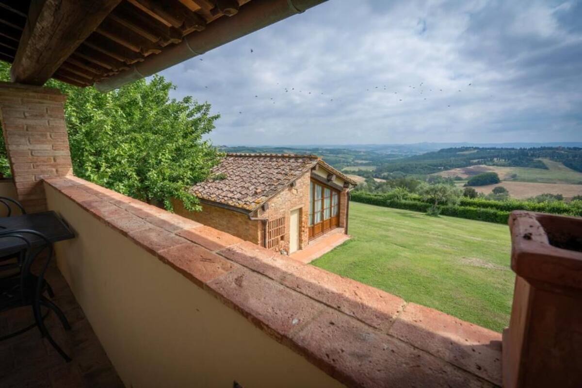 A balcony with a view of a rural landscape, a brick wall, and a small building with a tiled roof.