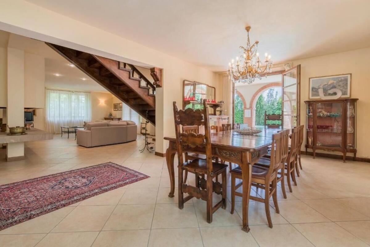 A spacious dining area with a wooden table and chairs, a chandelier, and a staircase leading to another room.