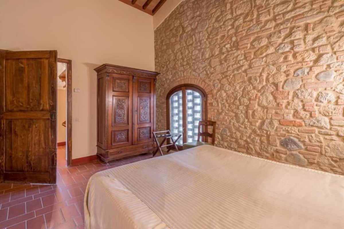 A bedroom with a stone wall, wooden wardrobe, and a bed.
