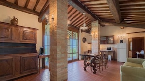 A rustic kitchen with wooden cabinets, a dining table, and a green sofa. - Santo Pietro Resort (San Gimignano)
